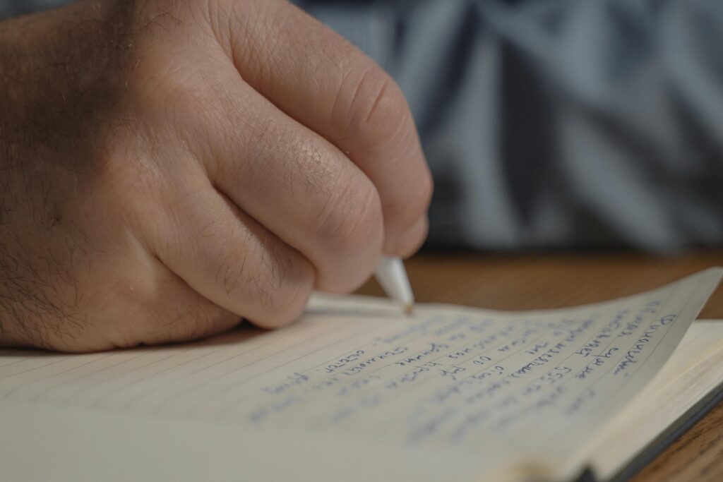 Close-up shot of an adult hand writing notes in a notebook with a pen.